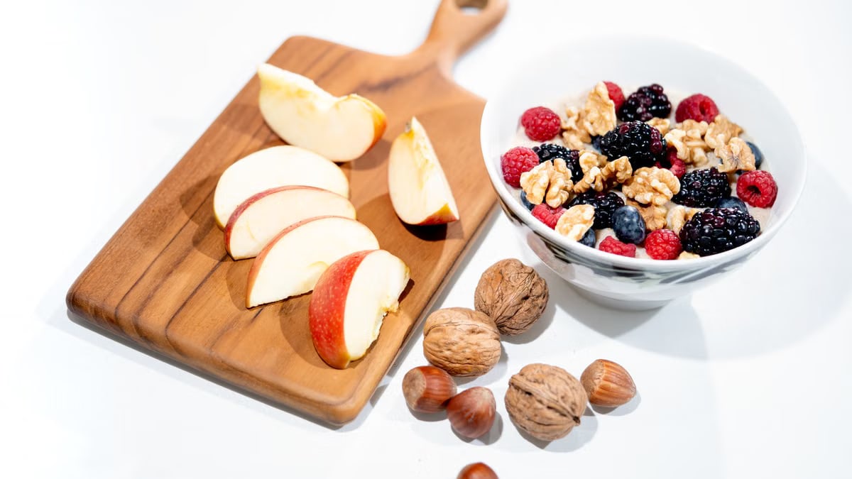 A vibrant breakfast bowl with mixed berries, walnuts, and apple slices on a rustic board.